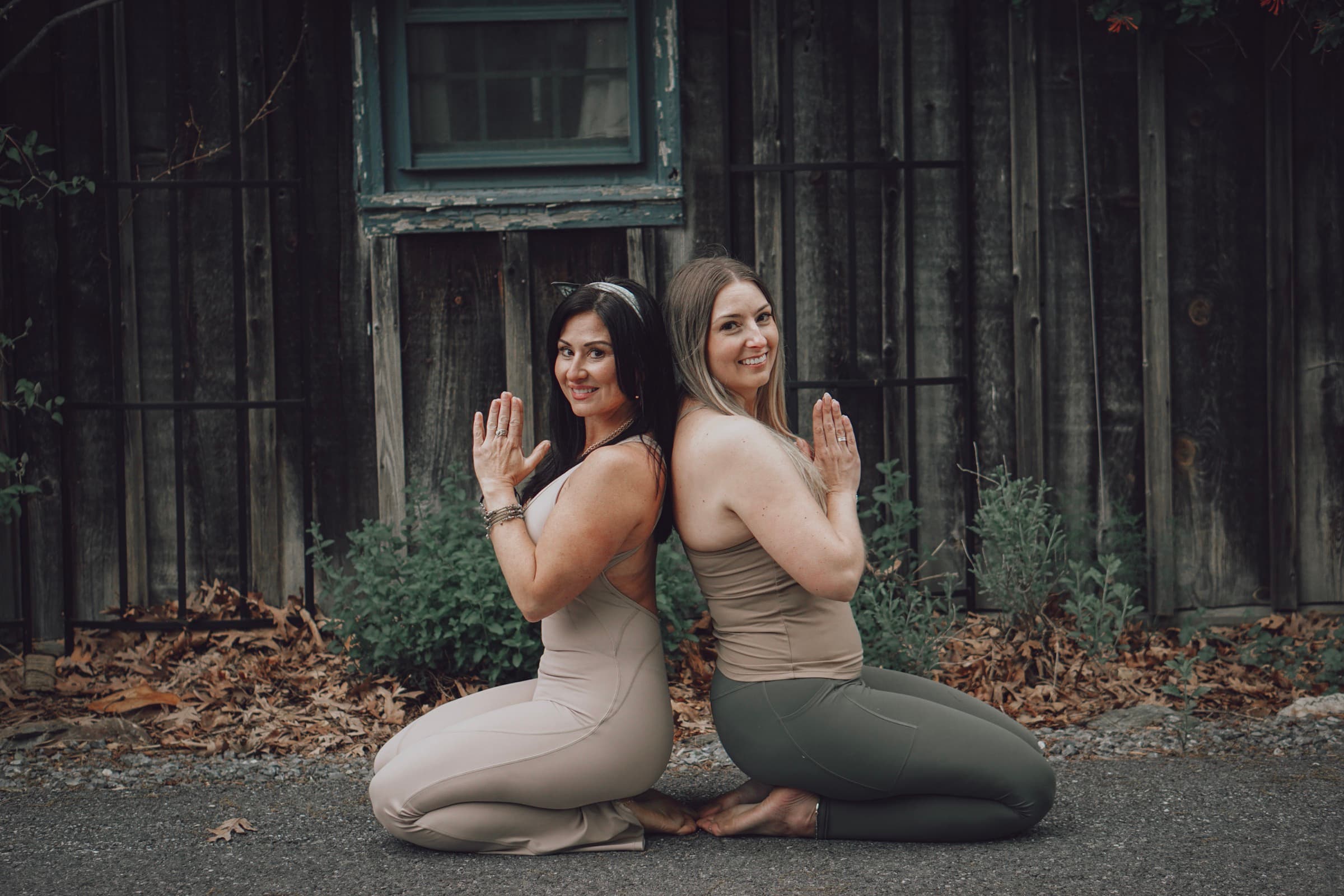 Sarah and Erin seated back-to-back in front of a rustic botanical wall.