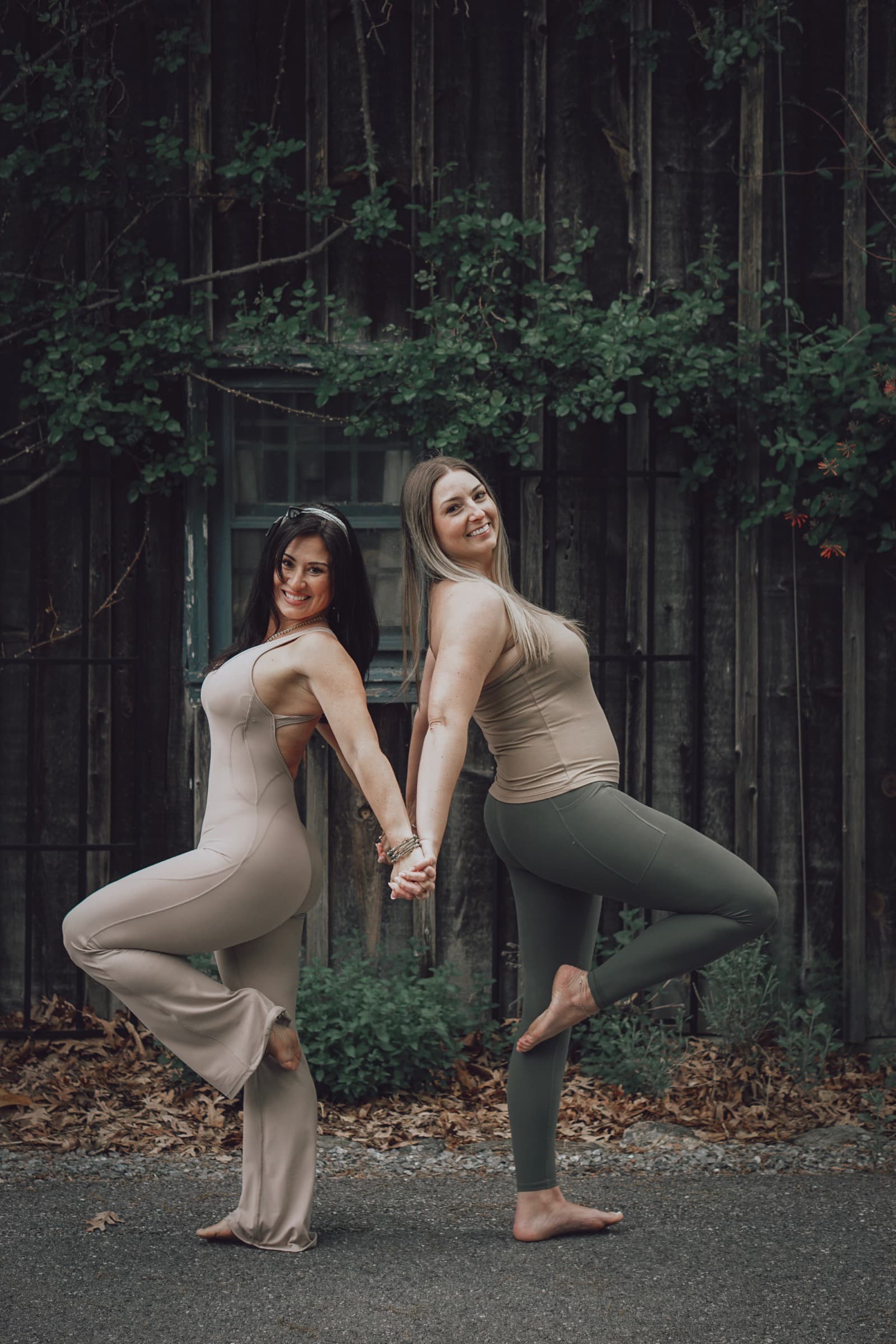Sarah and Erin holding hands in tree pose with one leg raised.